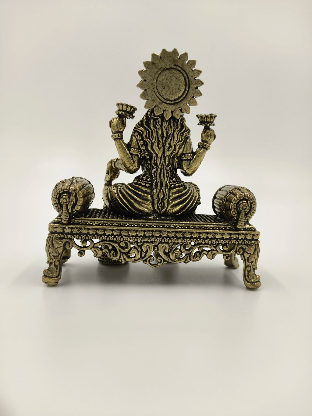 Back view of small brass Lakshmi statue seated on ornate platform