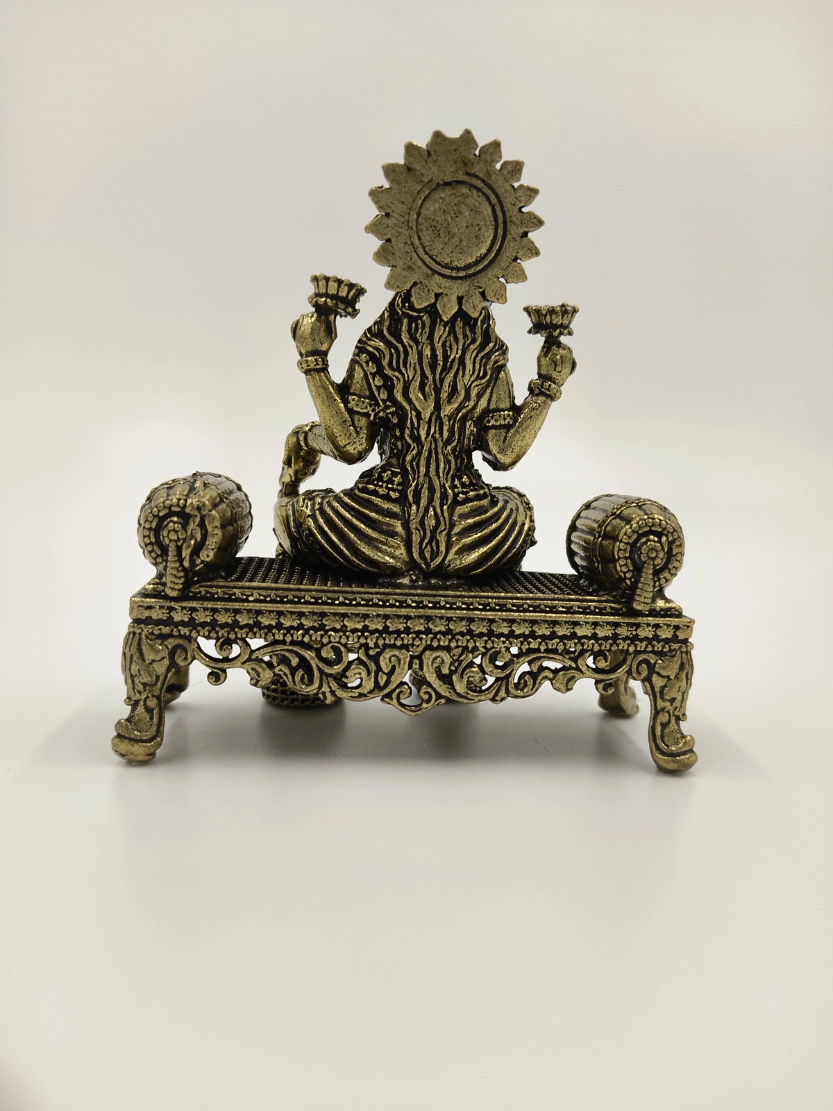 Back view of small brass Lakshmi statue seated on ornate platform