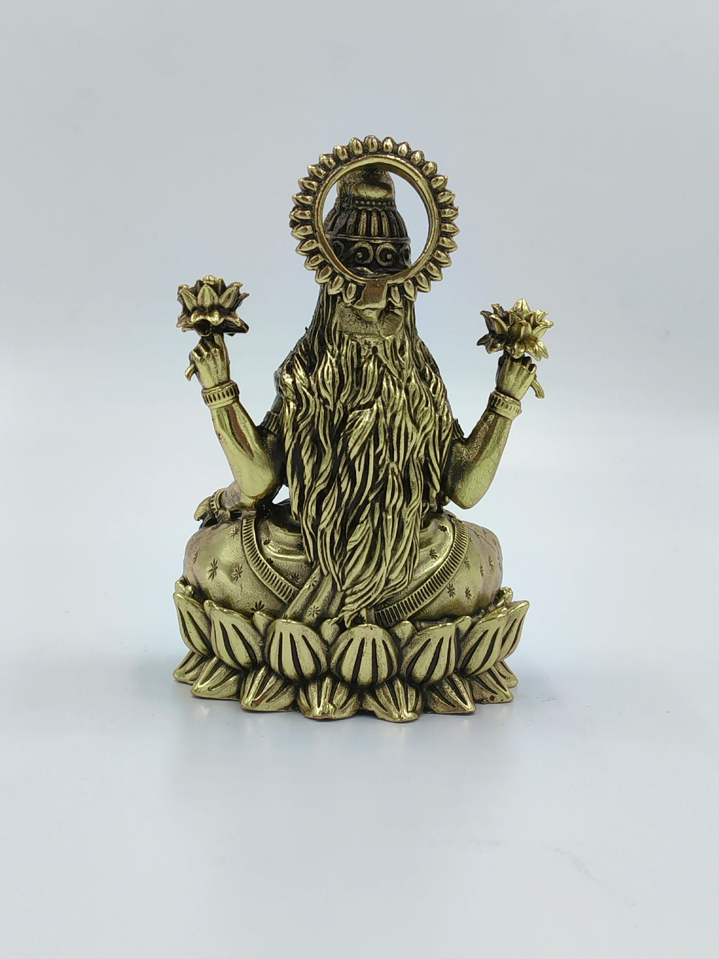 Back view of small brass Lakshmi idol seated on a lotus base holding lotus flowers
