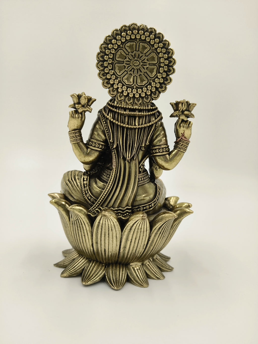 Back view of brass Lakshmi idol seated on lotus pedestal holding lotus flowers