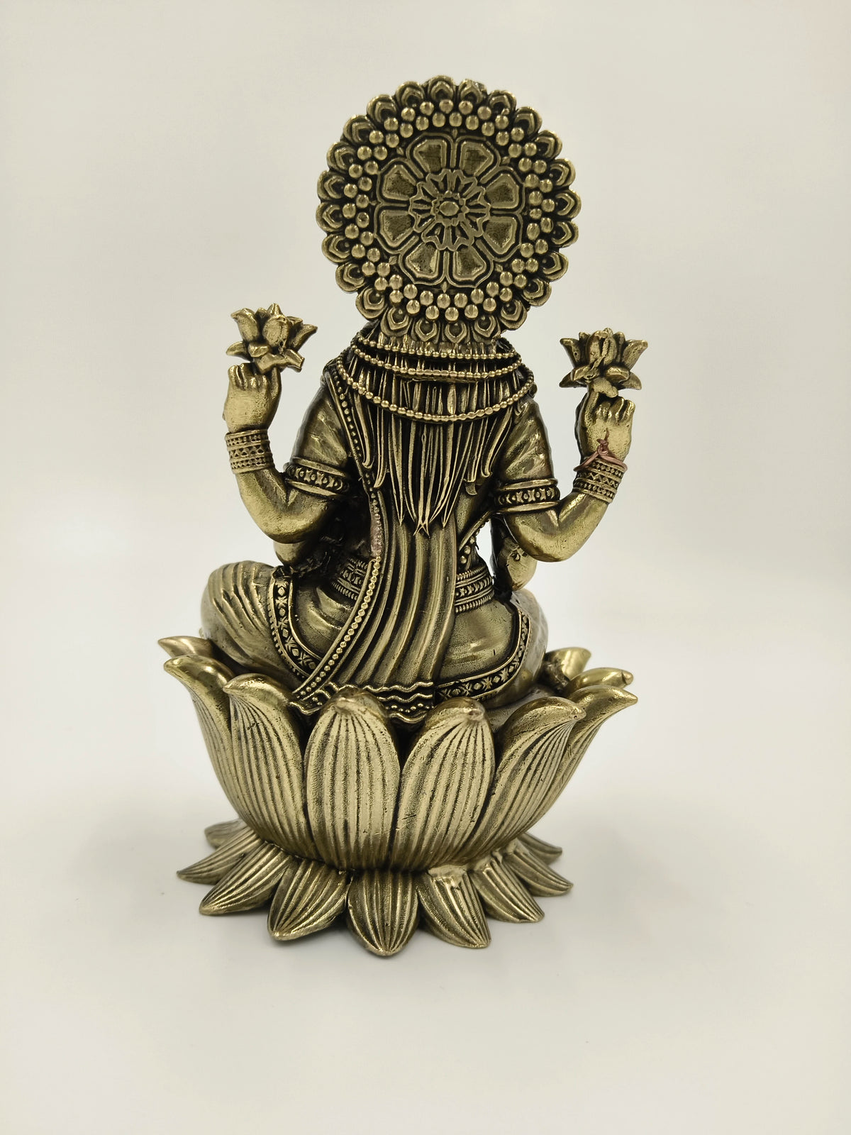Back view of brass Lakshmi idol seated on lotus pedestal holding lotus flowers