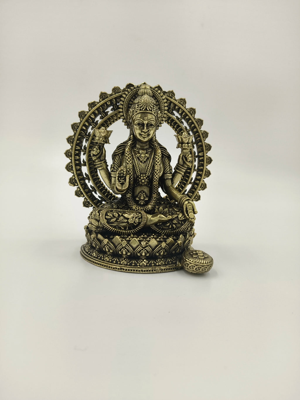 Small brass sculpture of Lakshmi seated inside a decorative arch