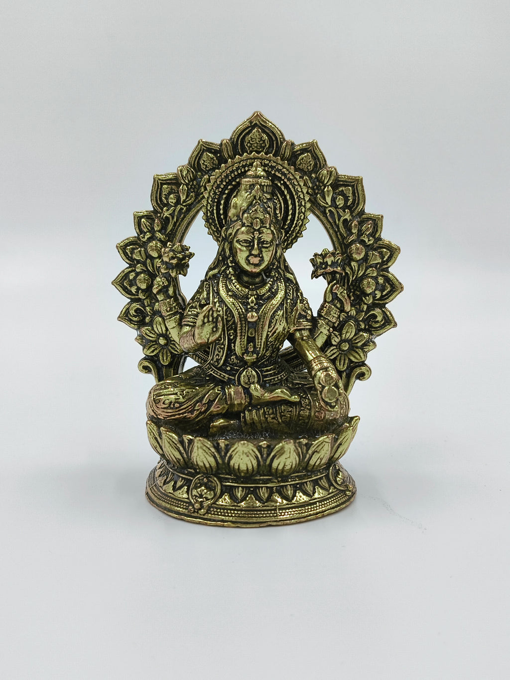 Small brass statue of Lakshmi deity seated with an ornate arch background