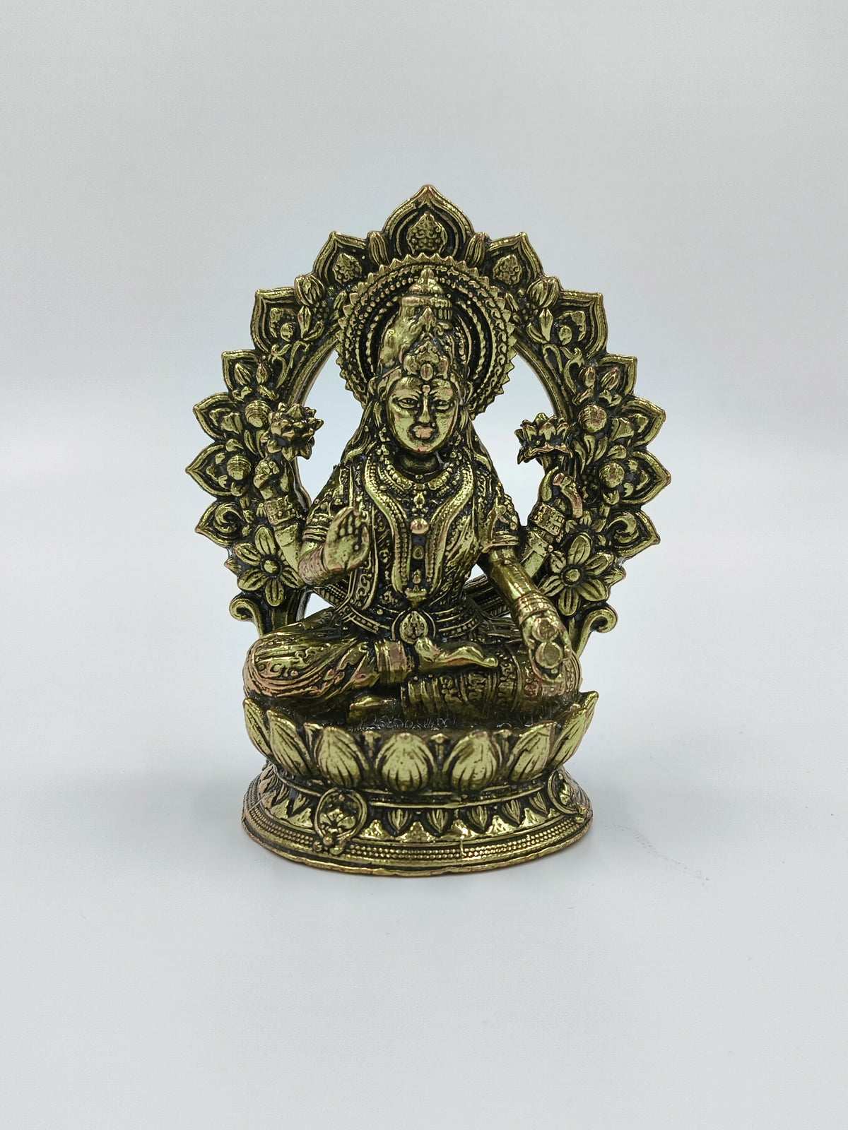 Small brass statue of Lakshmi deity seated with an ornate arch background