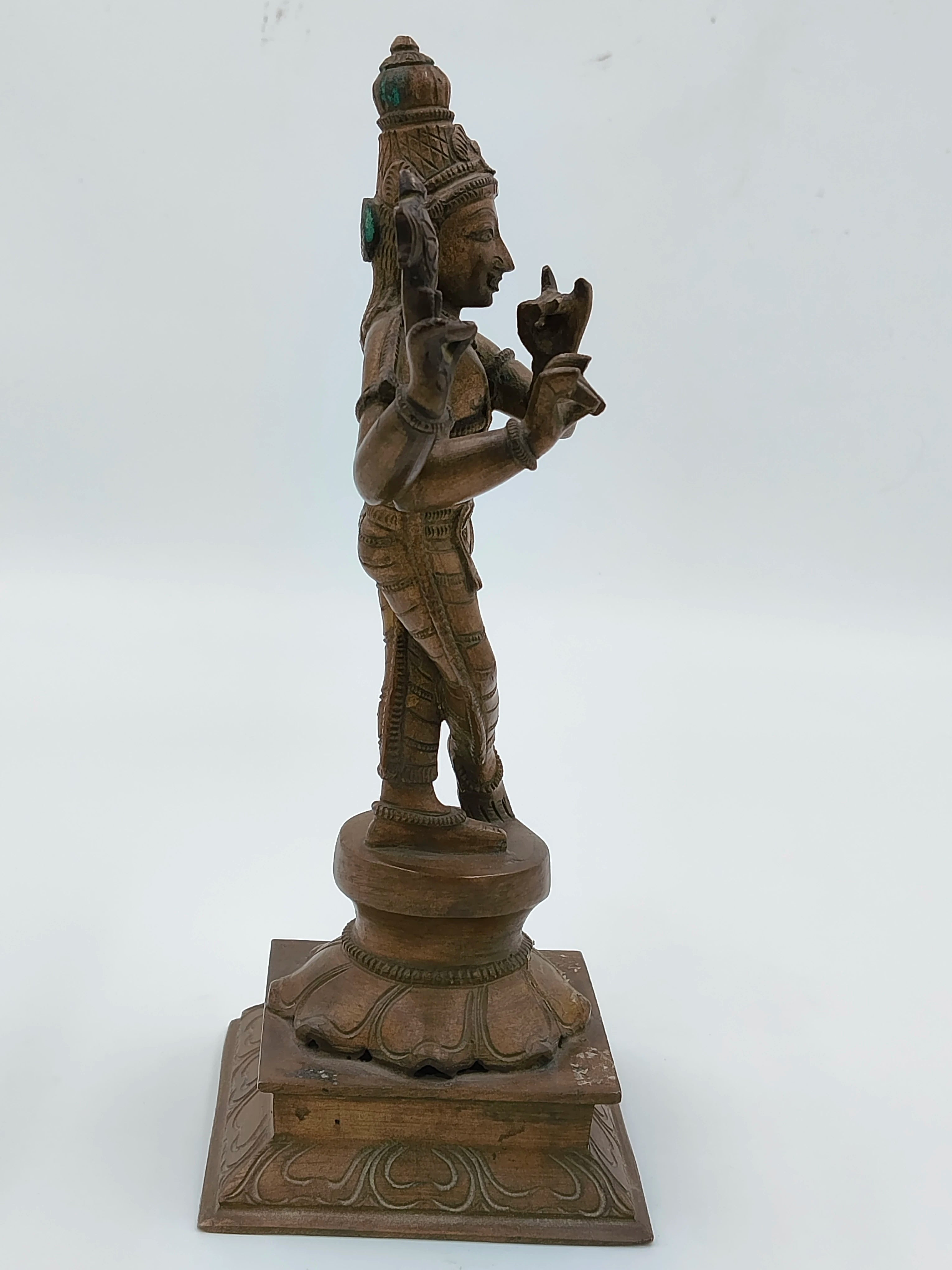 Side view of a large bronze Krishna statue standing on decorated base