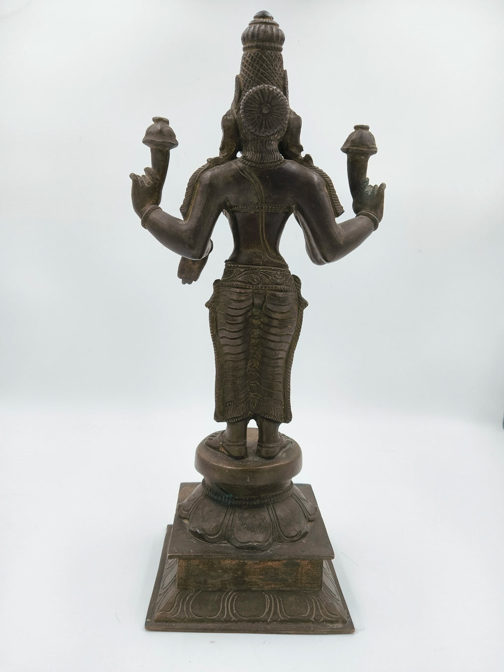 Back view of a large bronze statue of deity Dhanvathari holding objects in multiple hands