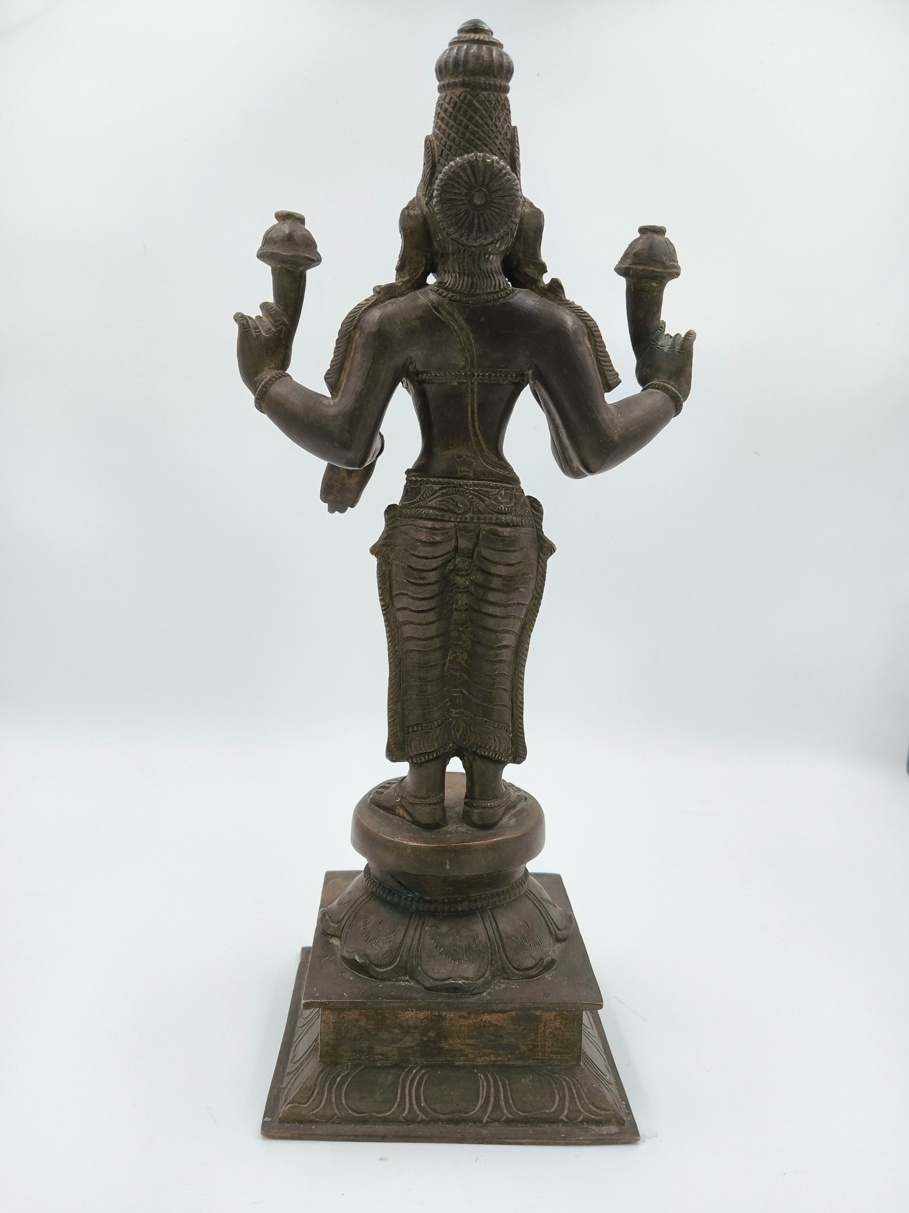 Back view of a large bronze statue of deity Dhanvathari holding objects in multiple hands