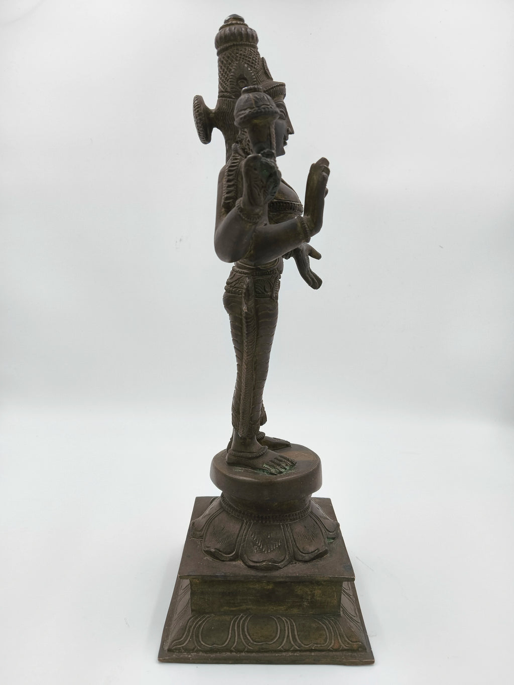 Side view of a large bronze Dhanvanthari deity sculpture standing on decorated pedestal
