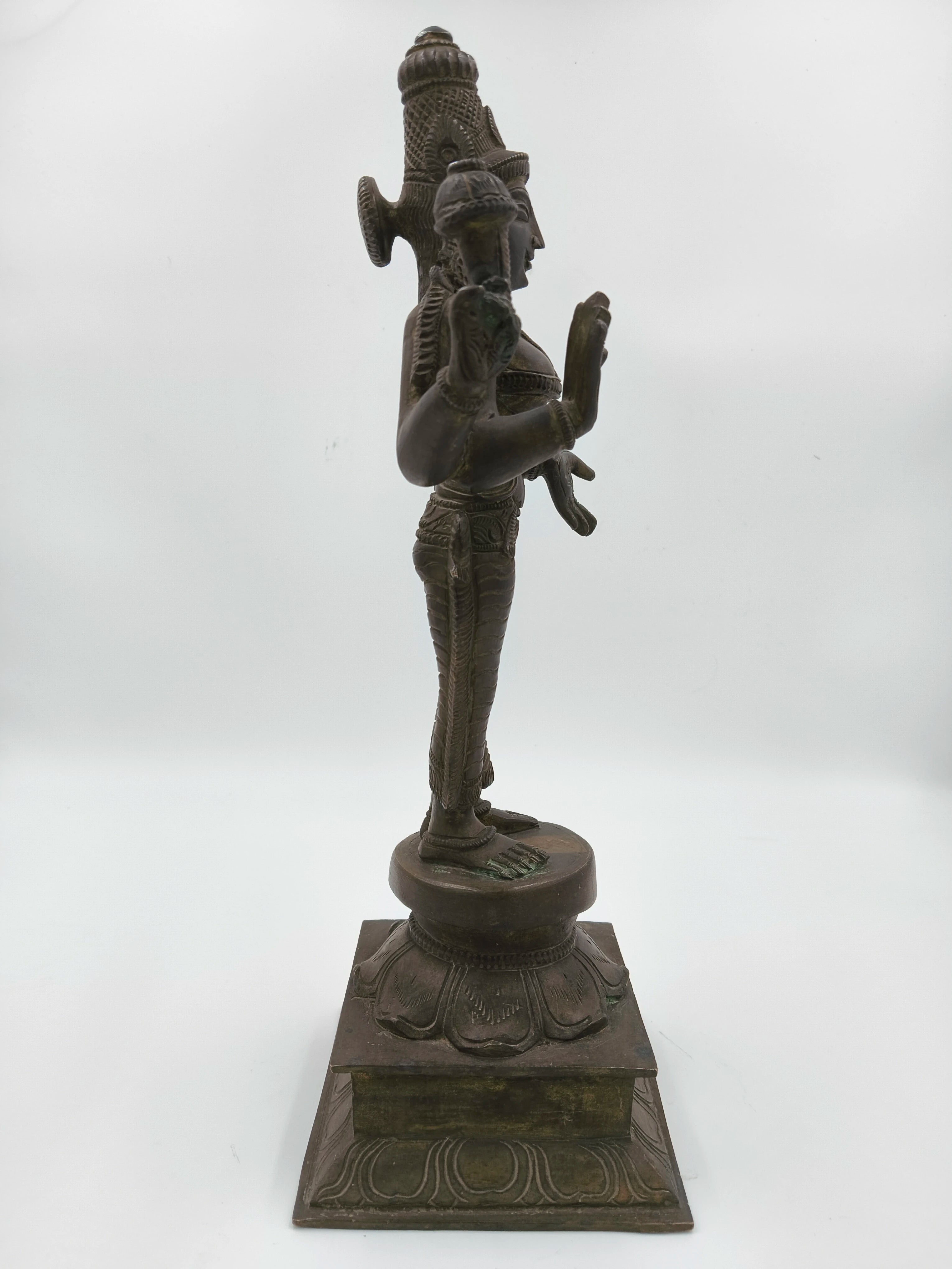 Side view of a large bronze Dhanvanthari deity sculpture standing on decorated pedestal