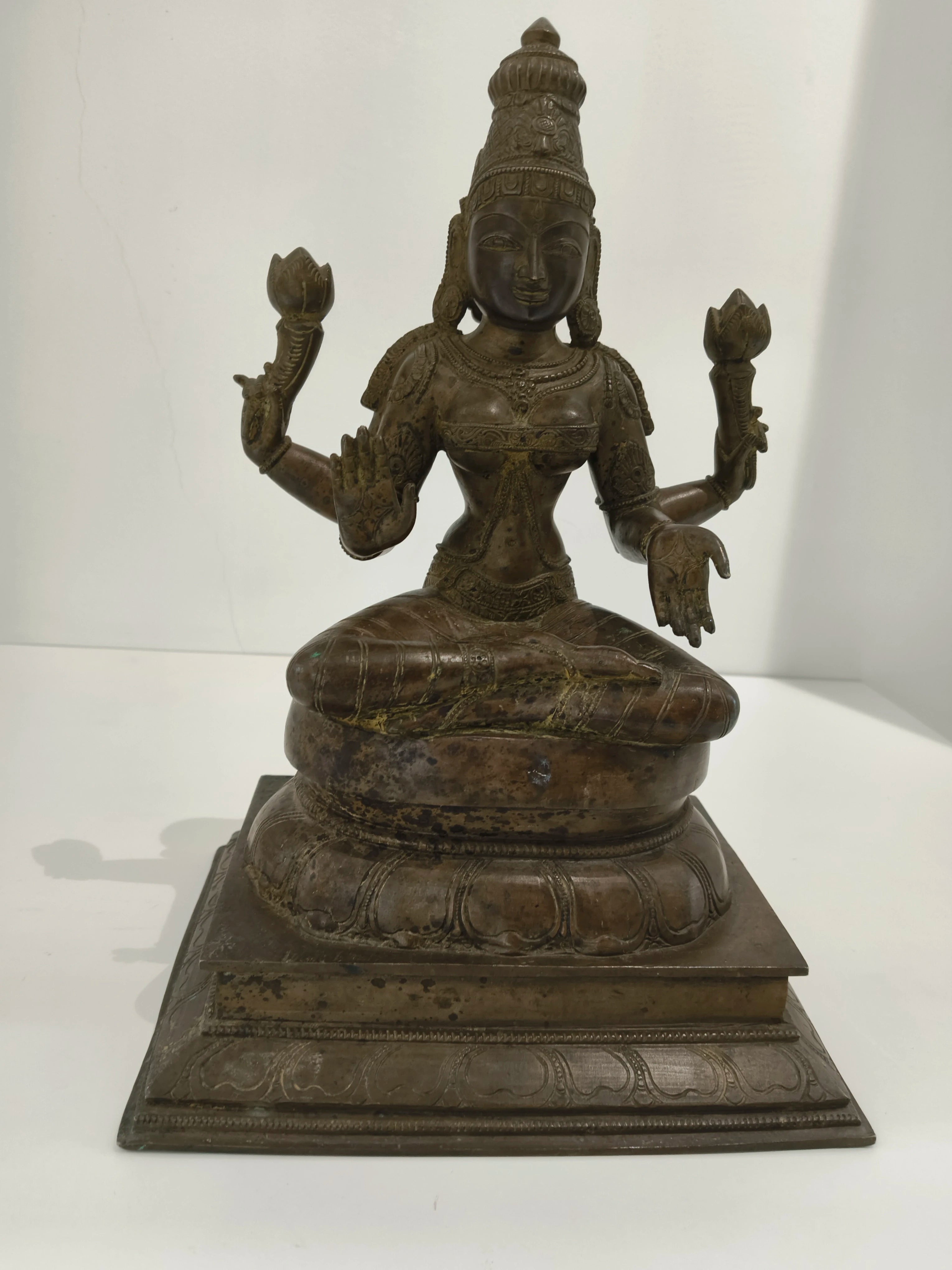 Large bronze Lakshmi statue seated with four arms holding lotus flowers on decorated base