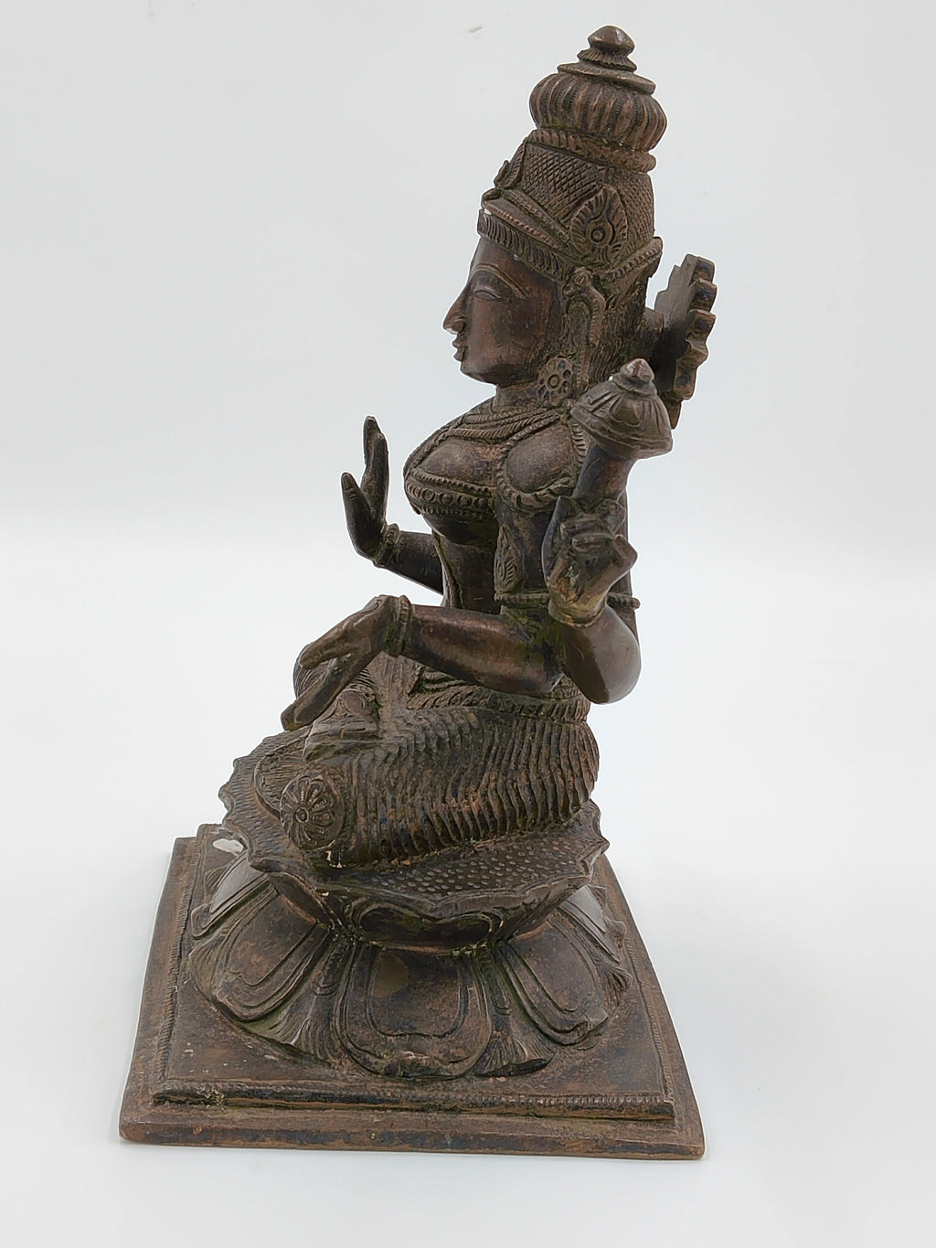 Side view of a large bronze statue of deity Lakshmi seated on lotus pedestal