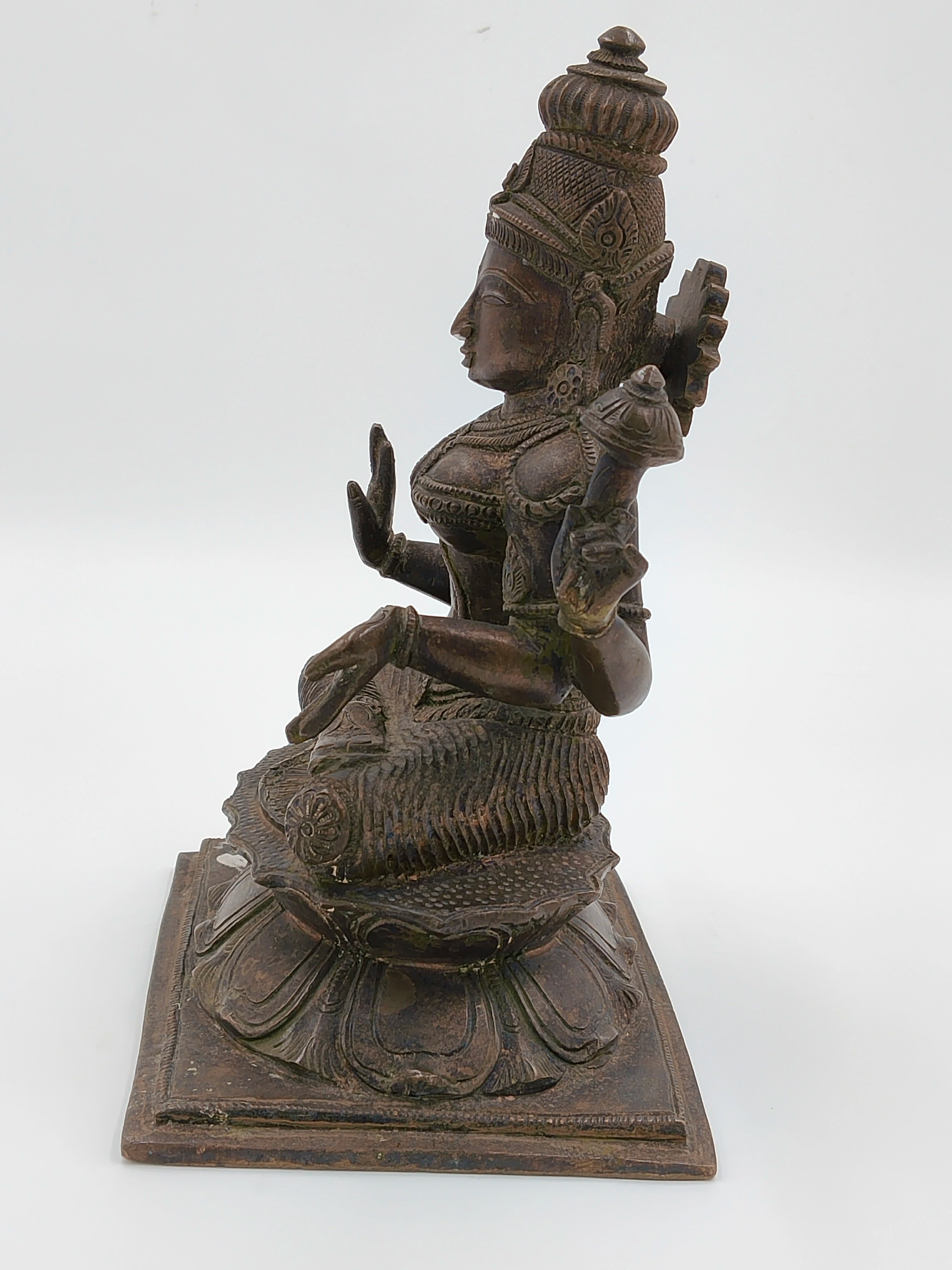 Side view of a large bronze statue of deity Lakshmi seated on lotus pedestal