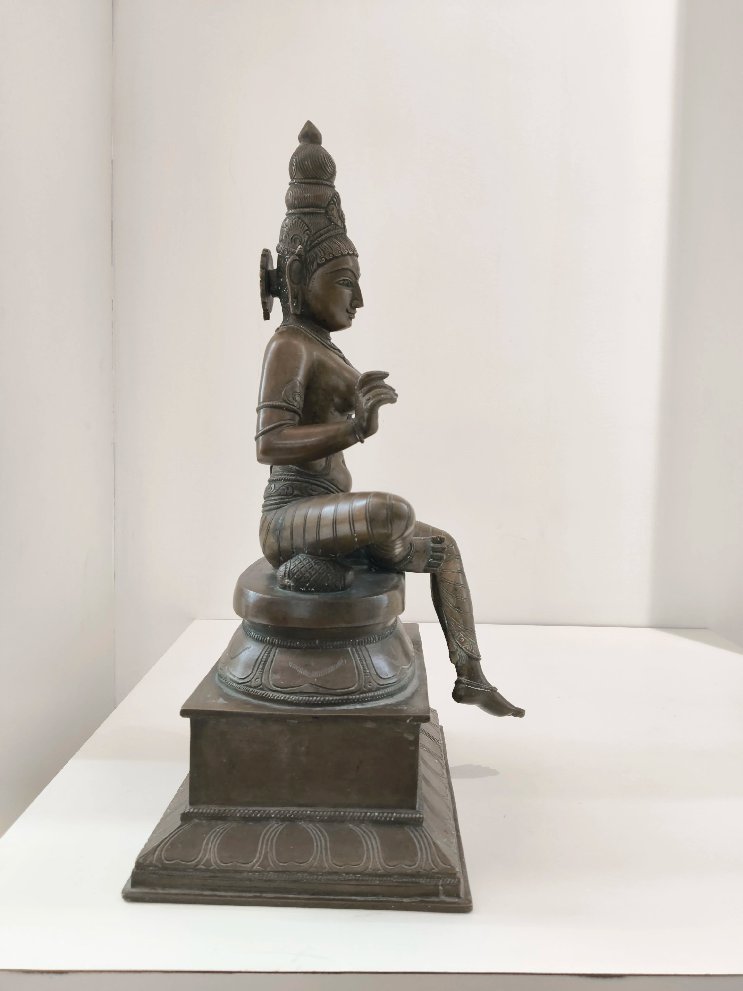 Large bronze statue of Parvathi deity seated on a decorative pedestal, side view
