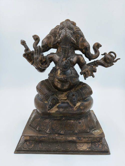 Bronze statue of four-faced Ganesh sitting on a decorated pedestal