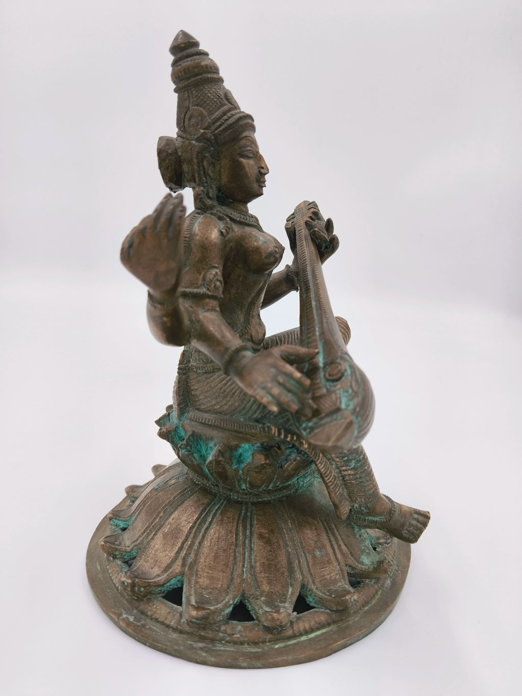 Side view of bronze Saraswathi sculpture playing veena on lotus base