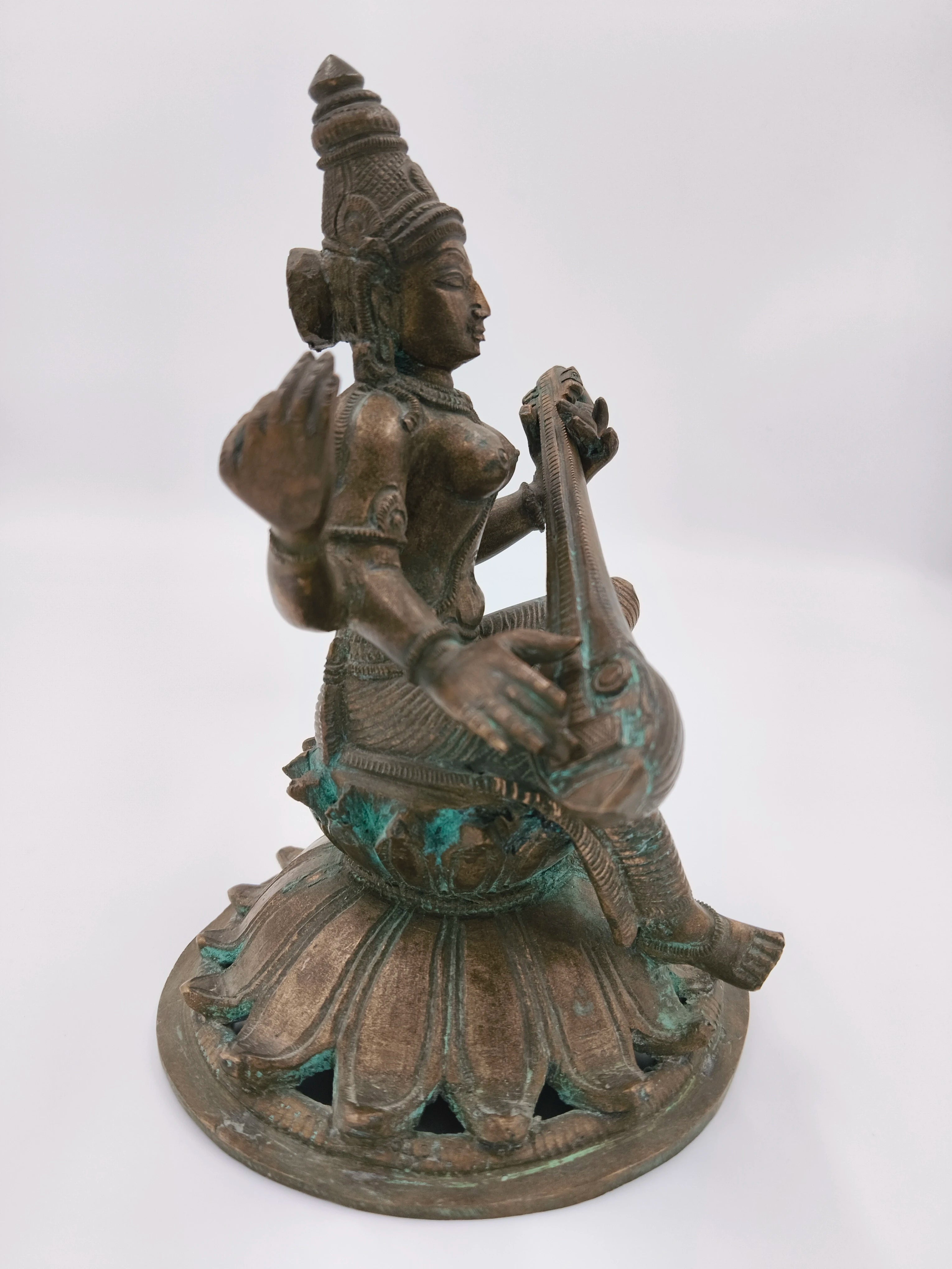 Side view of bronze Saraswathi sculpture playing veena on lotus base