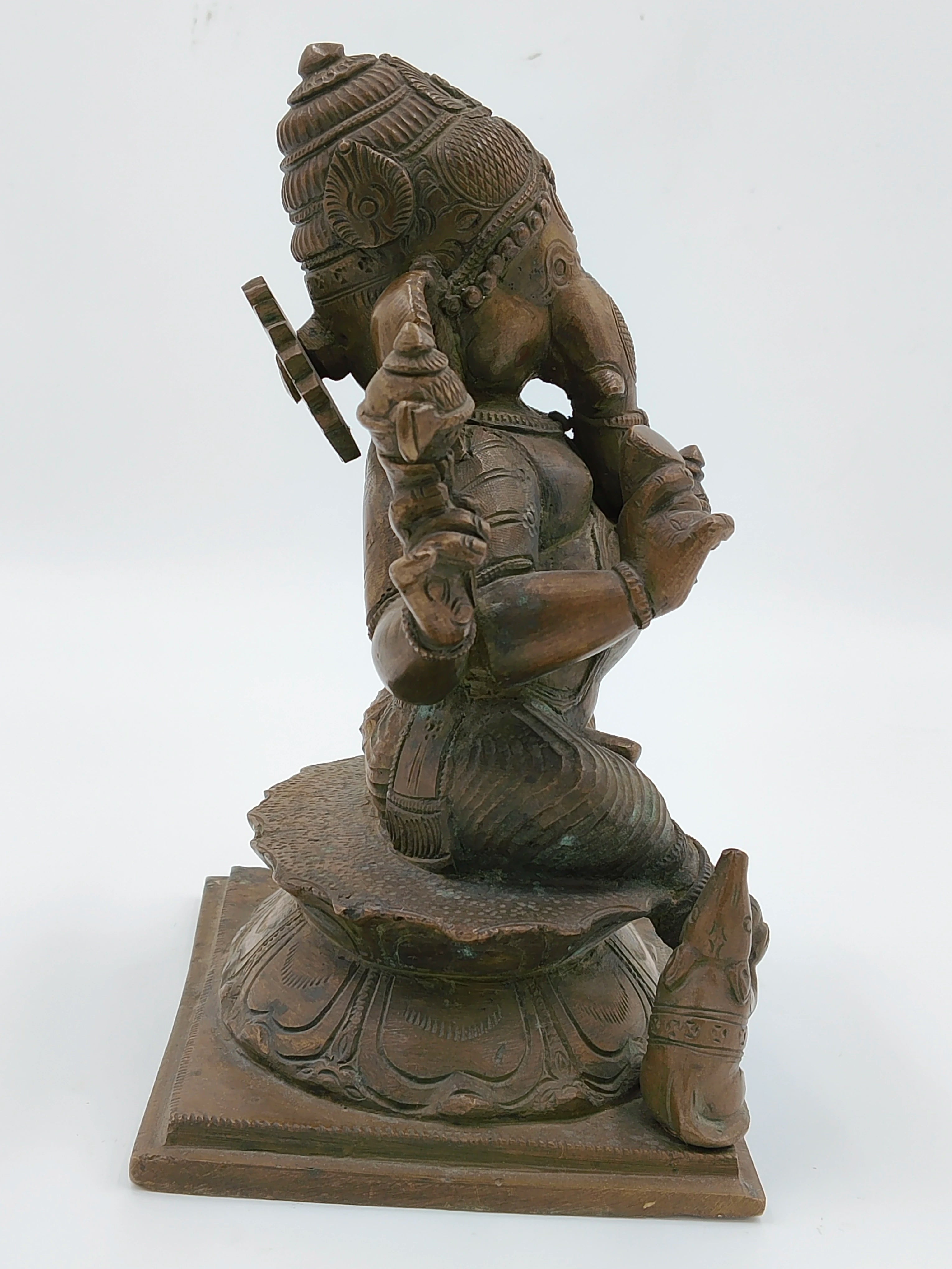 Side view of bronze Ganesh statue seated on decorated base with mouse figure