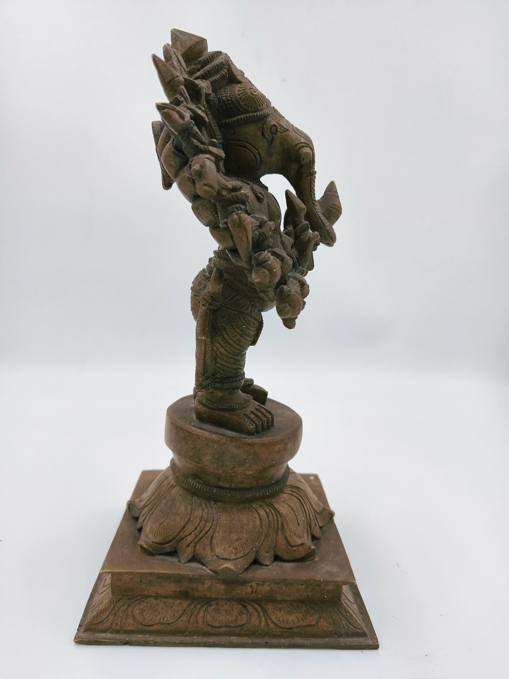 Side view of a large bronze Ganesh statue standing on a decorative base
