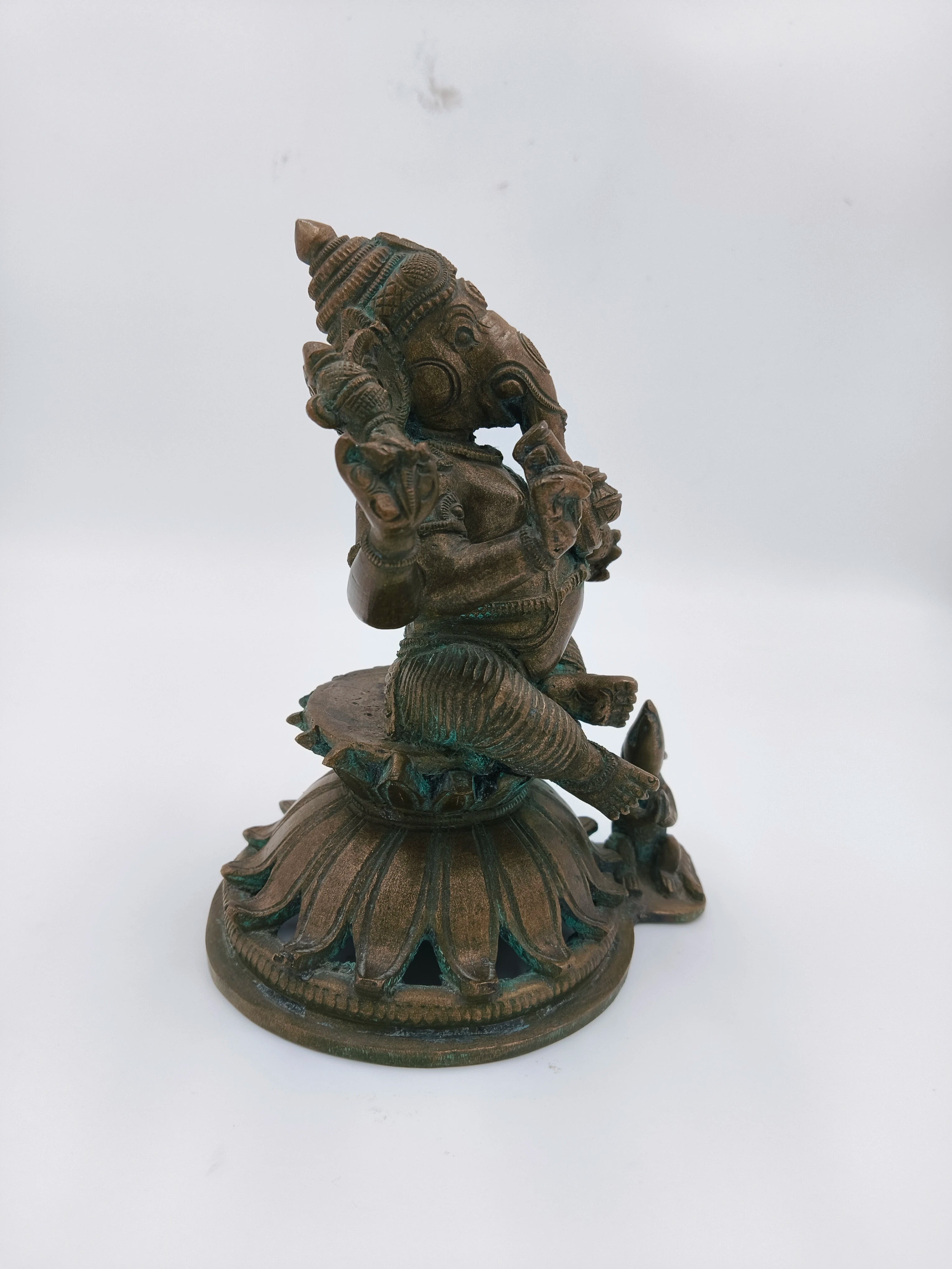 Side view of bronze Ganesh statue seated on lotus base with mice detail