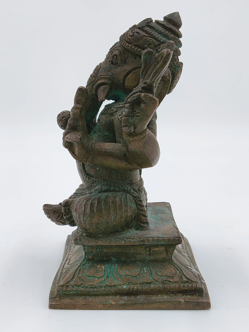 Side view of a bronze Ganesh statue seated on an ornate pedestal
