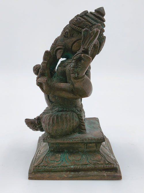 Side view of a bronze Ganesh statue seated on an ornate pedestal