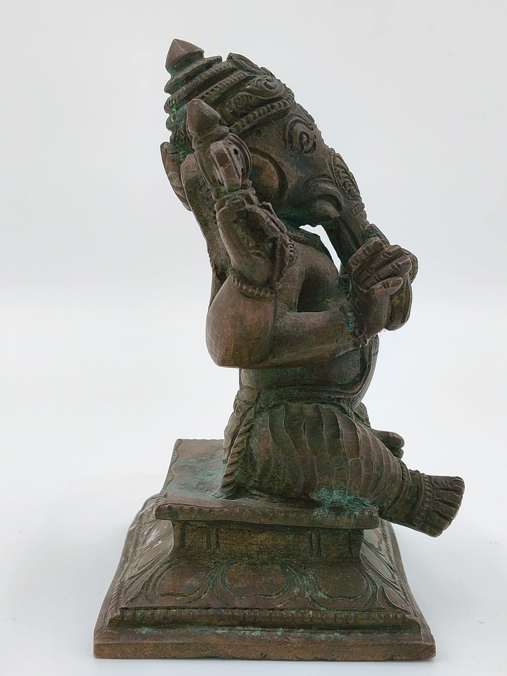 Side view of a bronze Ganesh statue seated on a decorated pedestal