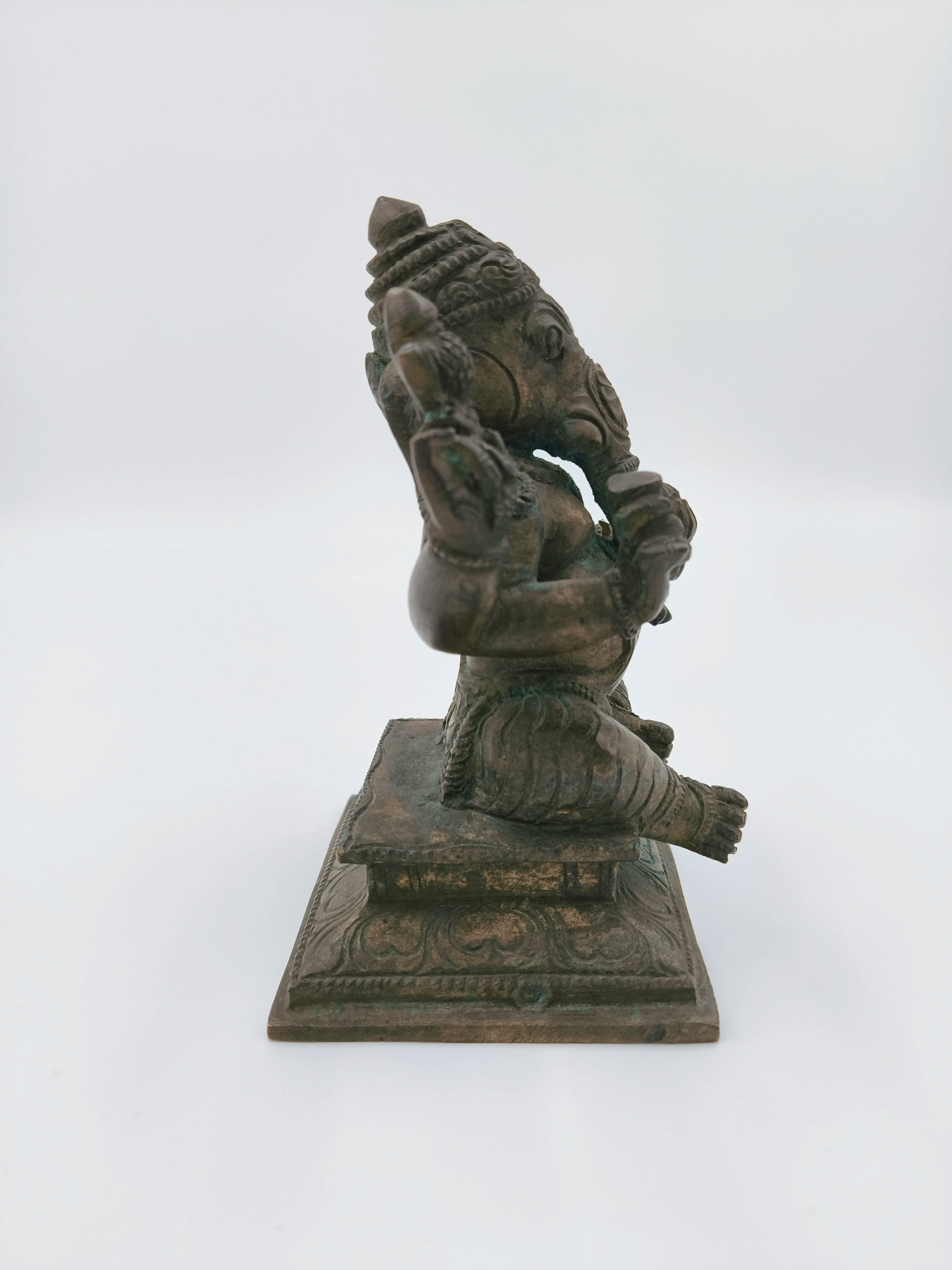 Side view of a bronze Ganesh statue sitting on a decorated base