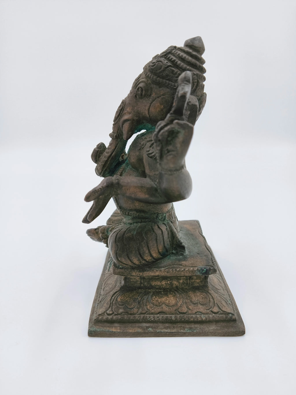 Side view of a bronze Ganesh statue seated on a decorative base