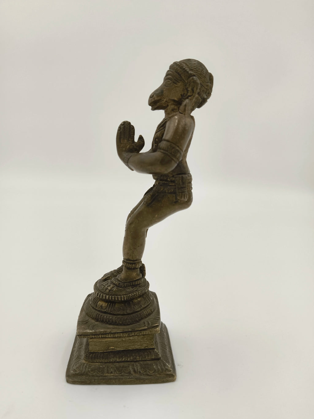 Side view of bronze Hanuman statue standing with folded hands on decorated base