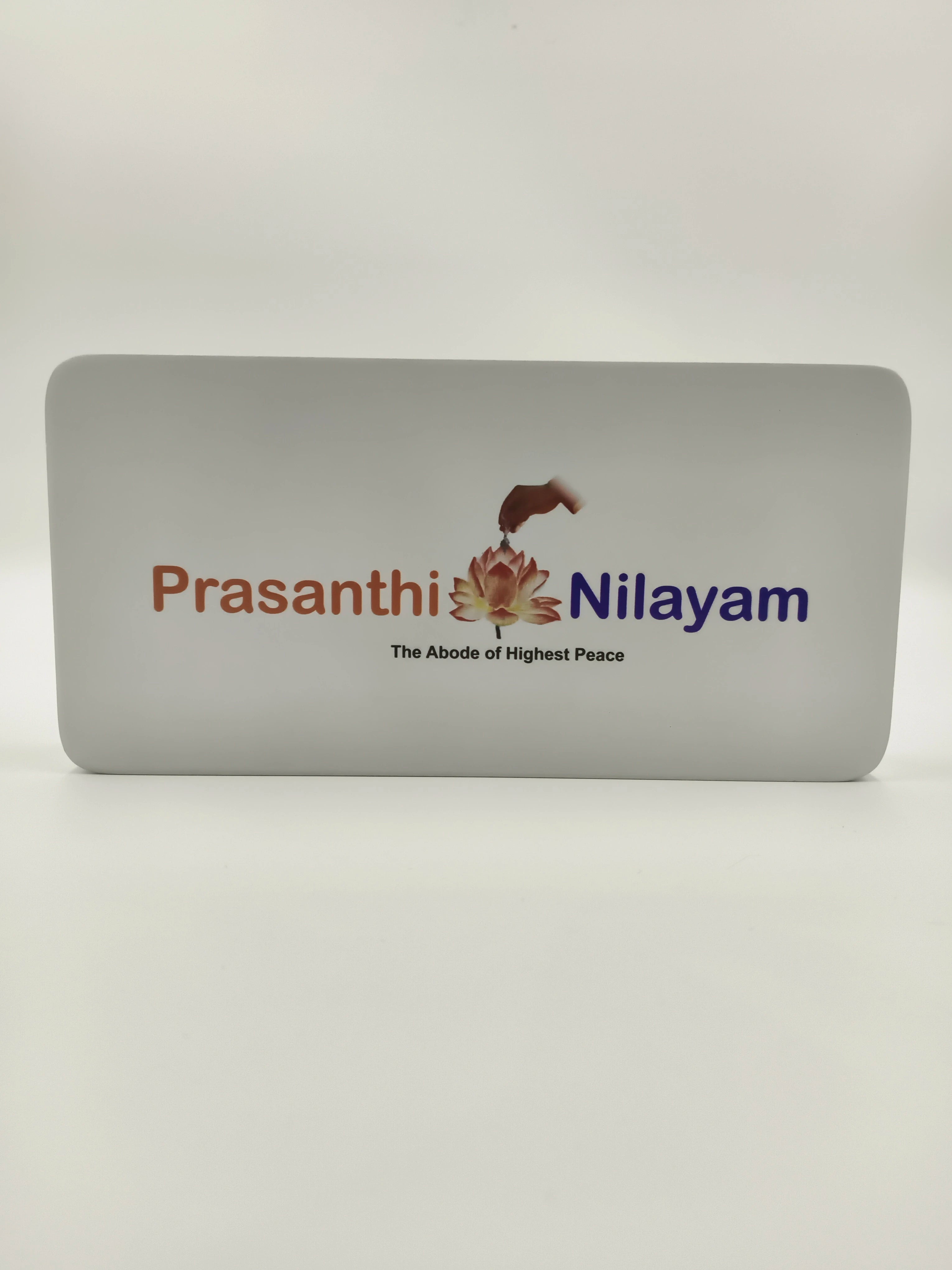 Small wooden tabletop clock featuring Prashanthi Nilayam logo and text