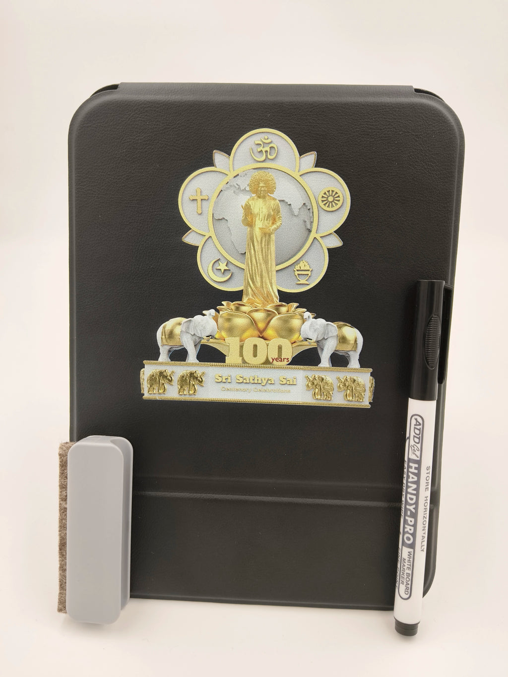 Black wooden board with Sri Sathya Sai Baba centenary logo, marker, and eraser