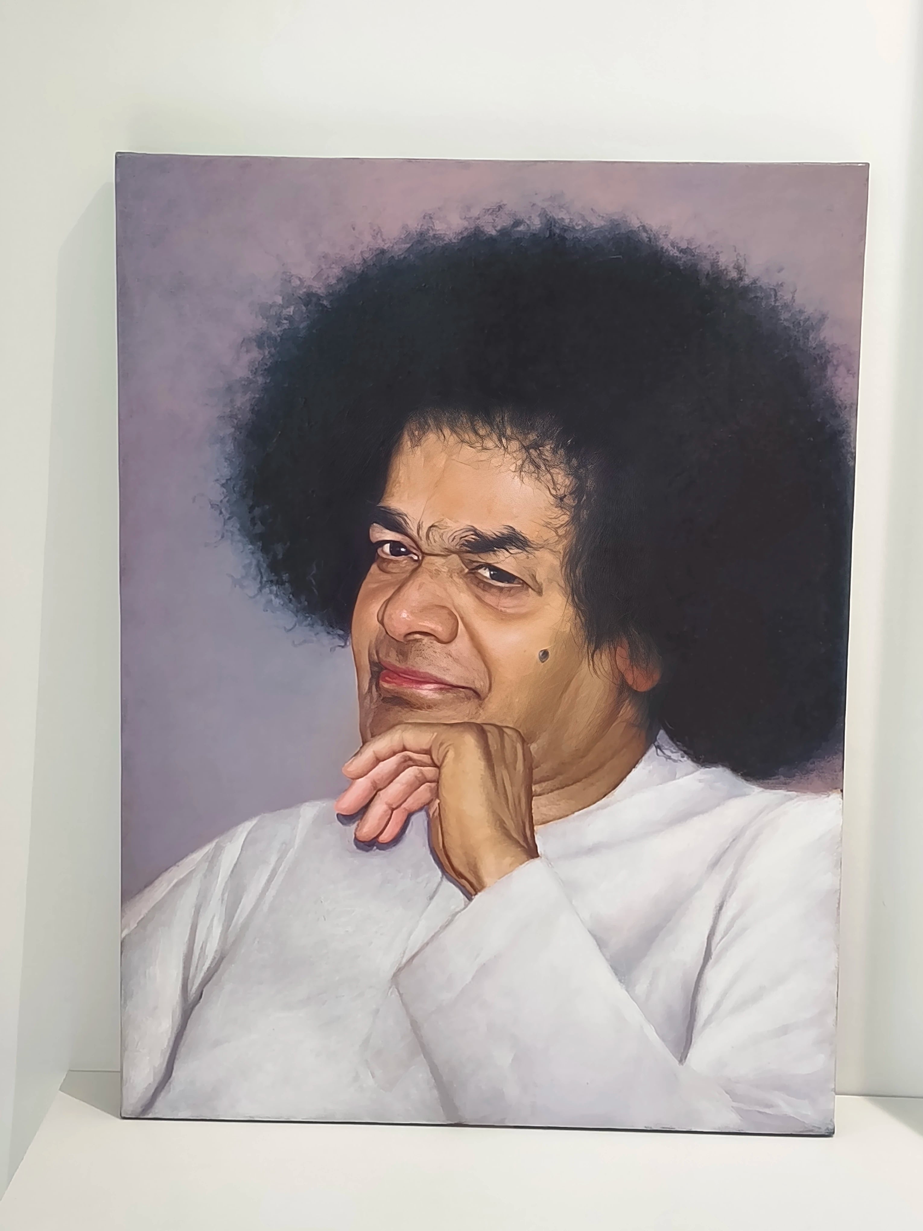 Large oil painting on canvas of Sai Baba with hand on chin against a muted background