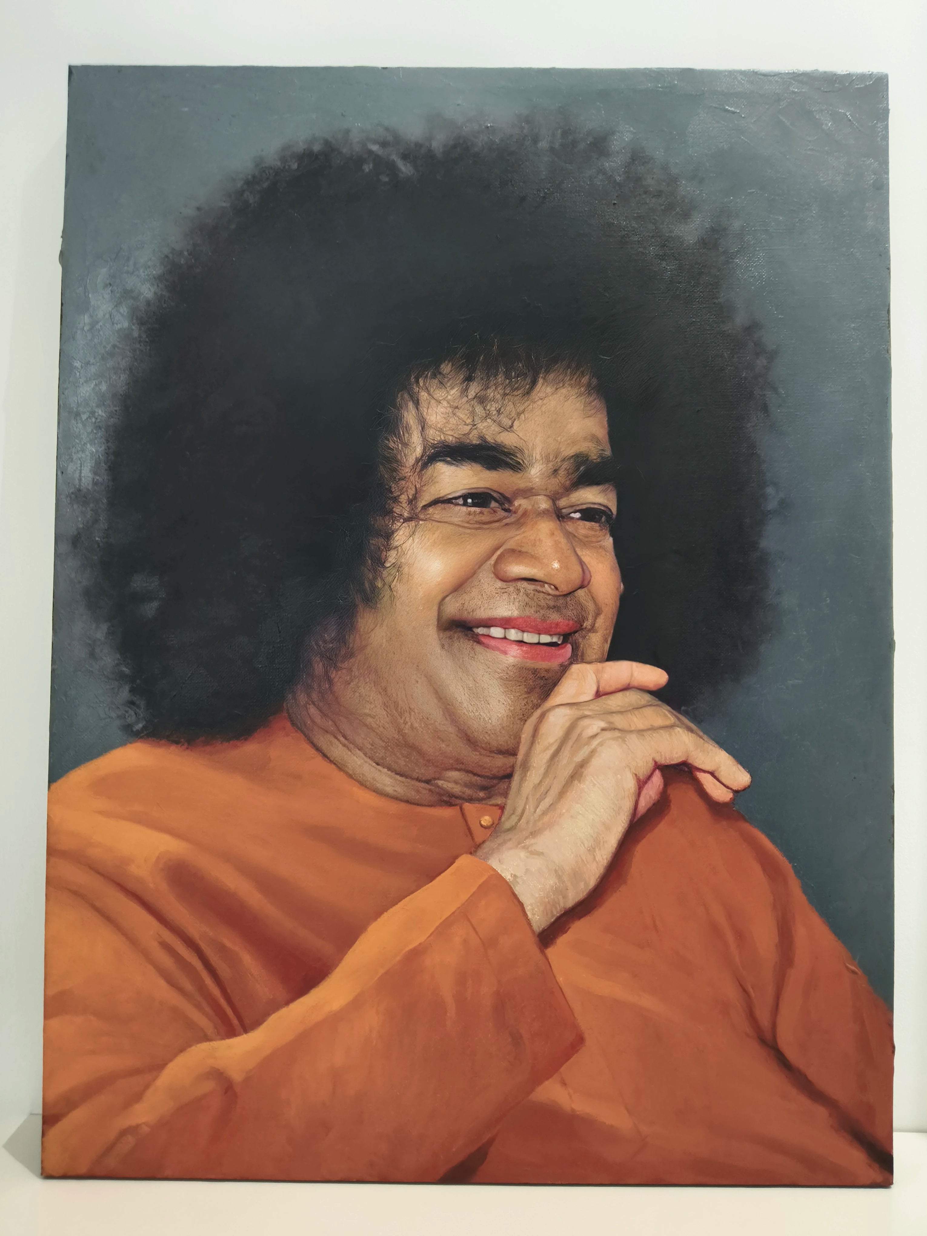 Large oil painting of Sai Baba in orange robe with smiling face and afro hairstyle on canvas