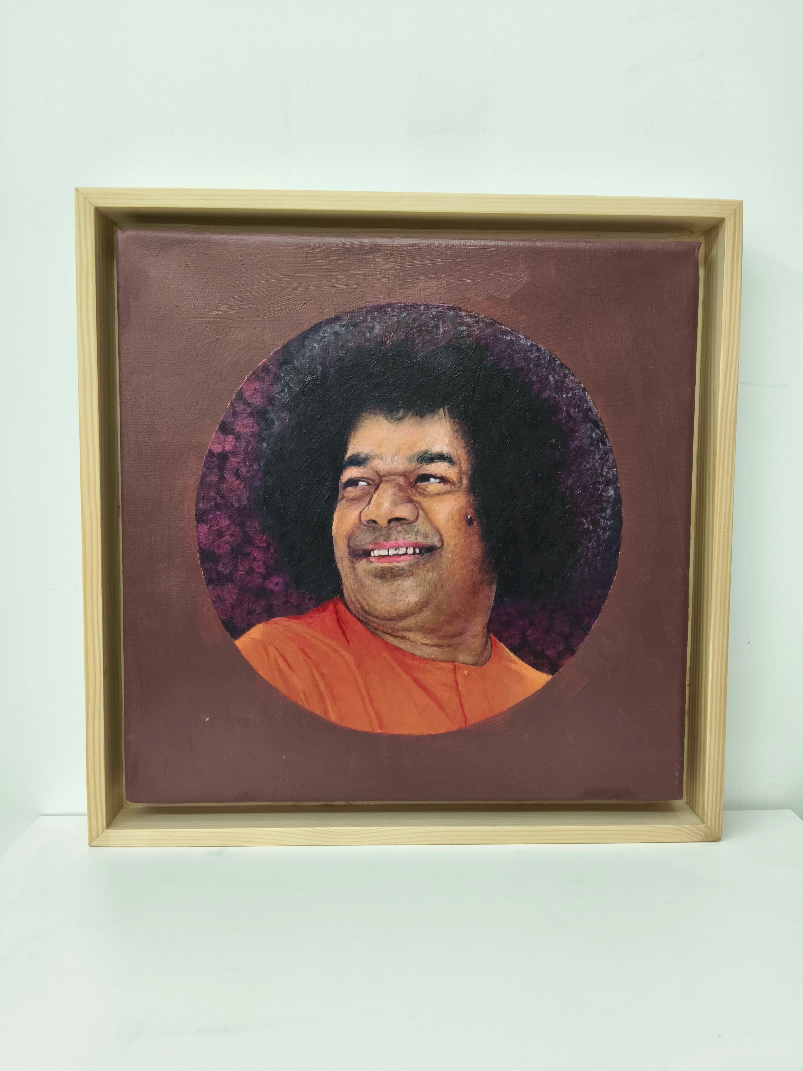 Framed oil painting portrait of Sai Baba with orange robe and dark curly hair
