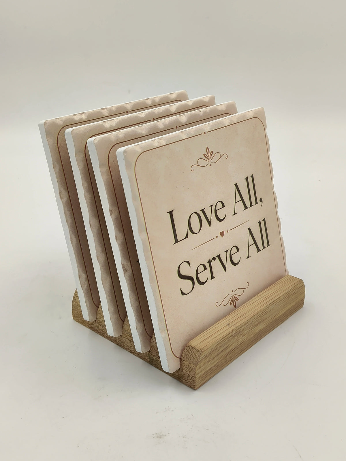 Set of ceramic coasters with 'Love All, Serve All' text on wooden holder