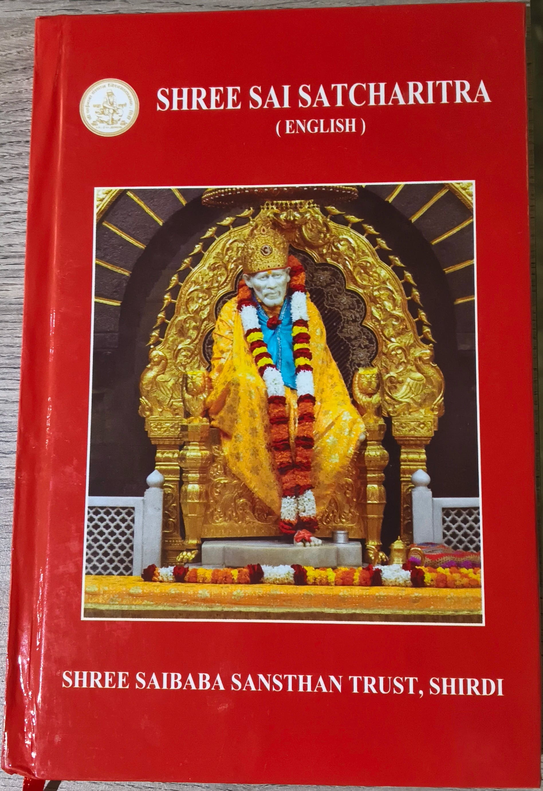 Sri Sai Satcharitra English paperback book with red cover and Sai Baba statue image